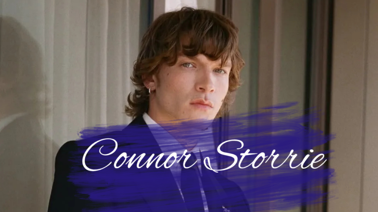 Connor Storrie smiling at a red carpet event in a black suit
